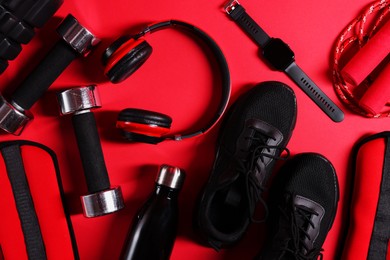 Photo of Different gym stuff, wrist watch and headphones on red background, flat lay