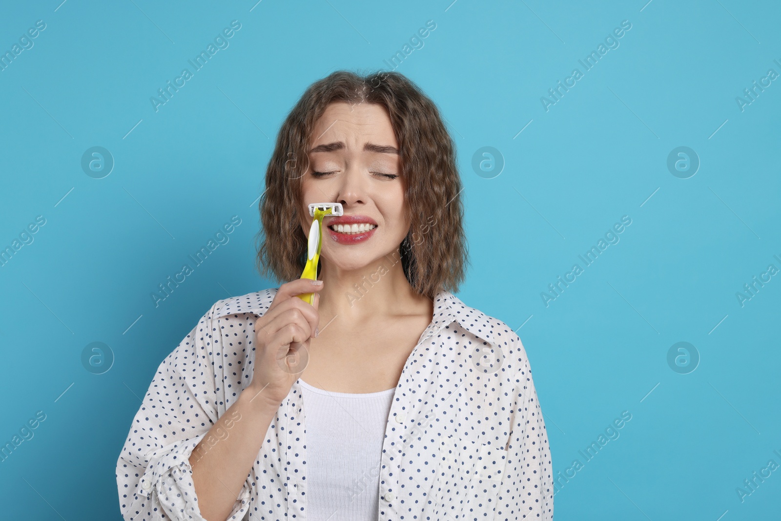 Photo of Emotional woman shaving her mustache with razor on light blue background