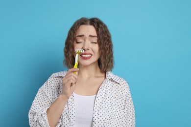 Emotional woman shaving her mustache with razor on light blue background