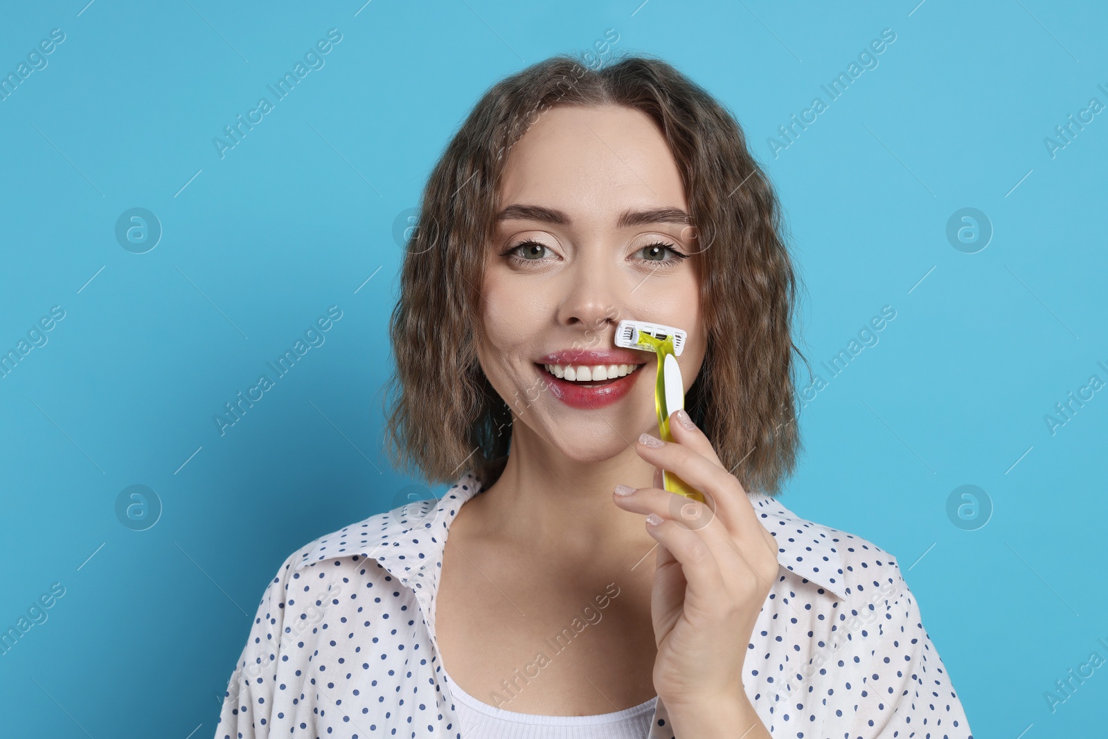 Photo of Smiling woman shaving her mustache with razor on light blue background