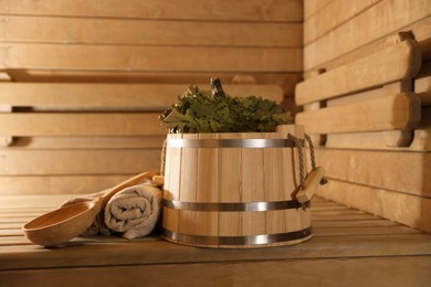 Photo of Bucket, whisk, ladle and towels on wooden bench in sauna