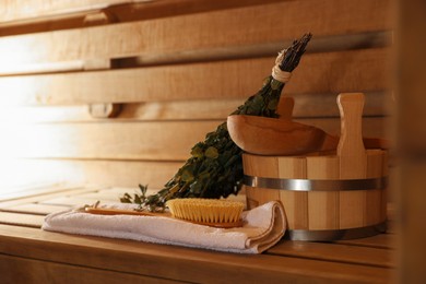 Massaging brush, towel, bucket, whisk and ladle on wooden bench in sauna