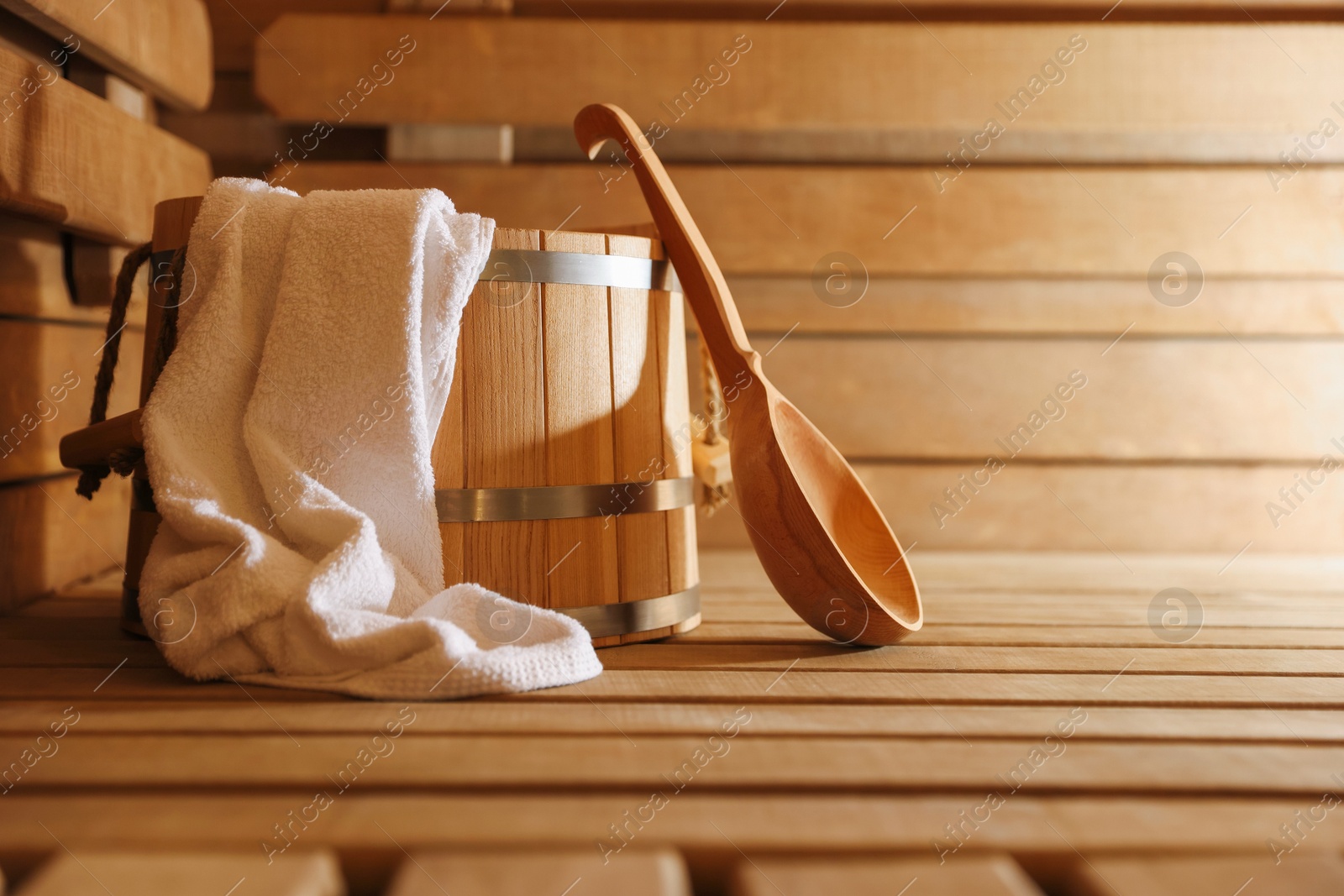 Photo of Bucket, ladle and towel on wooden bench in sauna. Space for text