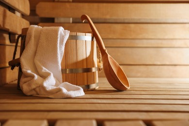 Photo of Bucket, ladle and towel on wooden bench in sauna. Space for text