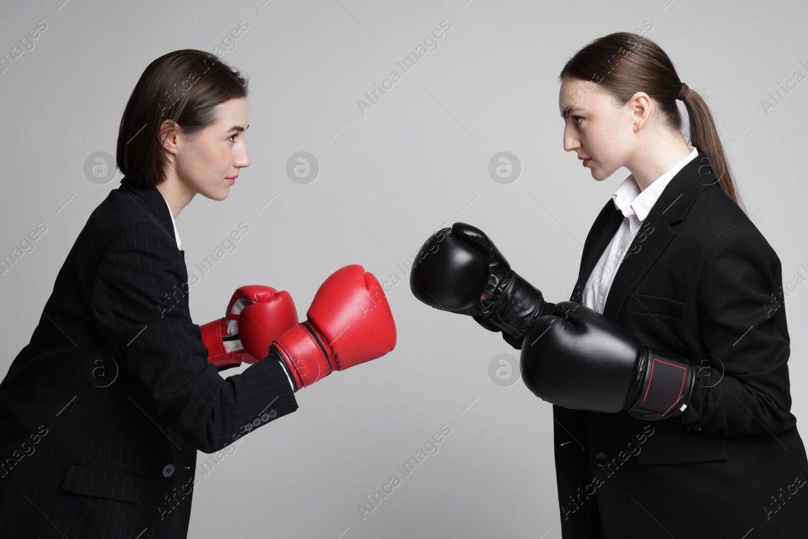 Photo of Competition. Businesswomen in gloves boxing on grey background