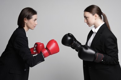 Photo of Competition. Businesswomen in gloves boxing on grey background