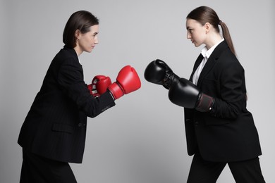 Competition. Businesswomen in gloves boxing on grey background