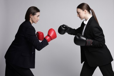 Photo of Competition. Businesswomen in gloves boxing on grey background