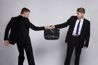 Photo of Competition concept. Businessmen pulling leather briefcase on grey background