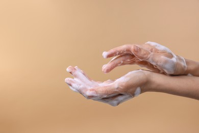 Photo of Woman washing hands with foaming soap on beige background, closeup with space for text. Hygiene