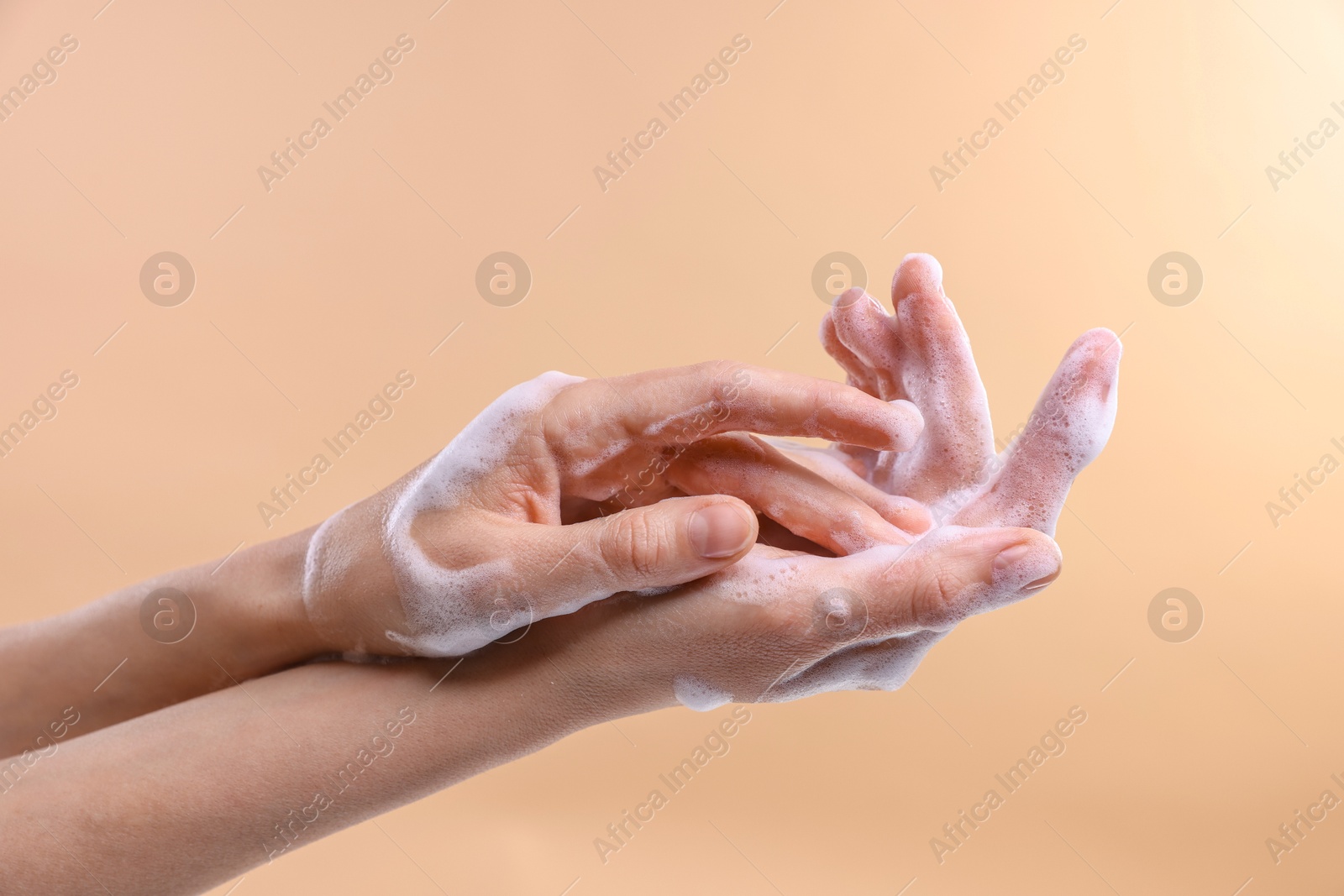 Photo of Woman washing hands with foaming soap on beige background, closeup. Hygiene