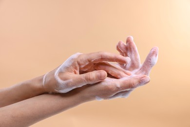 Woman washing hands with foaming soap on beige background, closeup. Hygiene