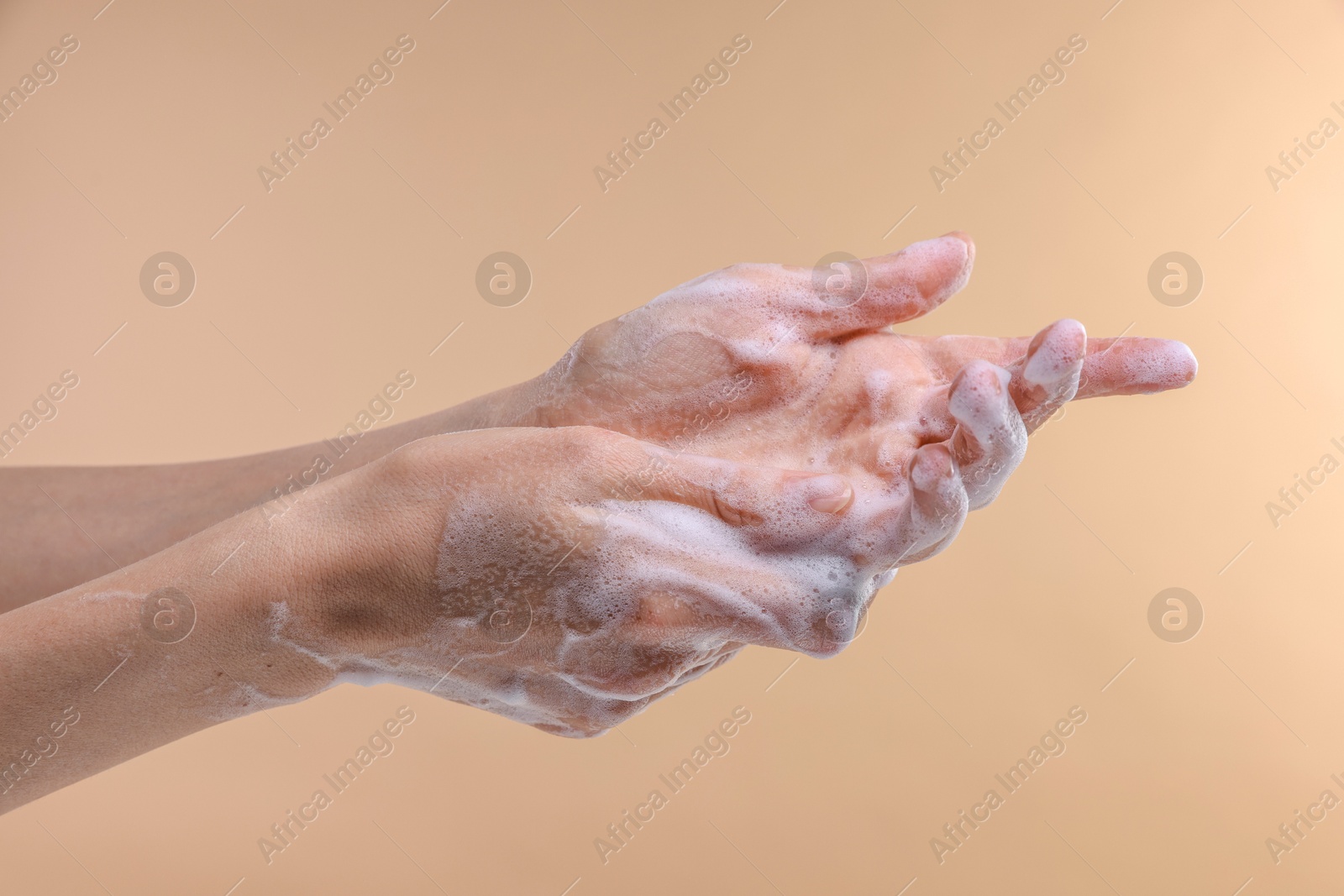 Photo of Woman washing hands with foaming soap on beige background, closeup. Hygiene