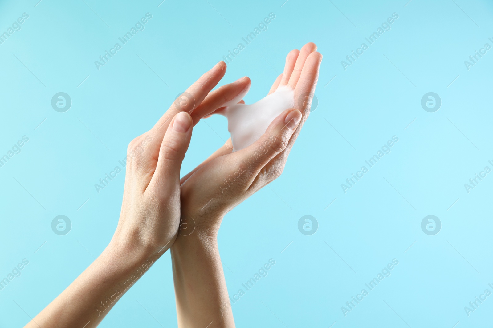 Photo of Woman washing hands with foaming soap on light blue background, closeup with space for text. Hygiene