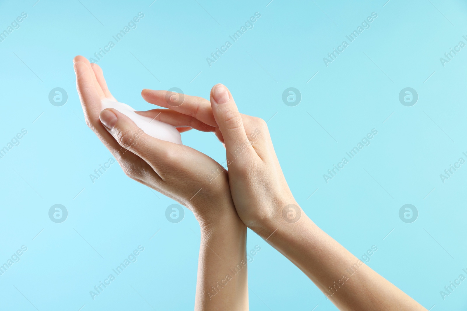 Photo of Woman washing hands with foaming soap on light blue background, closeup. Hygiene