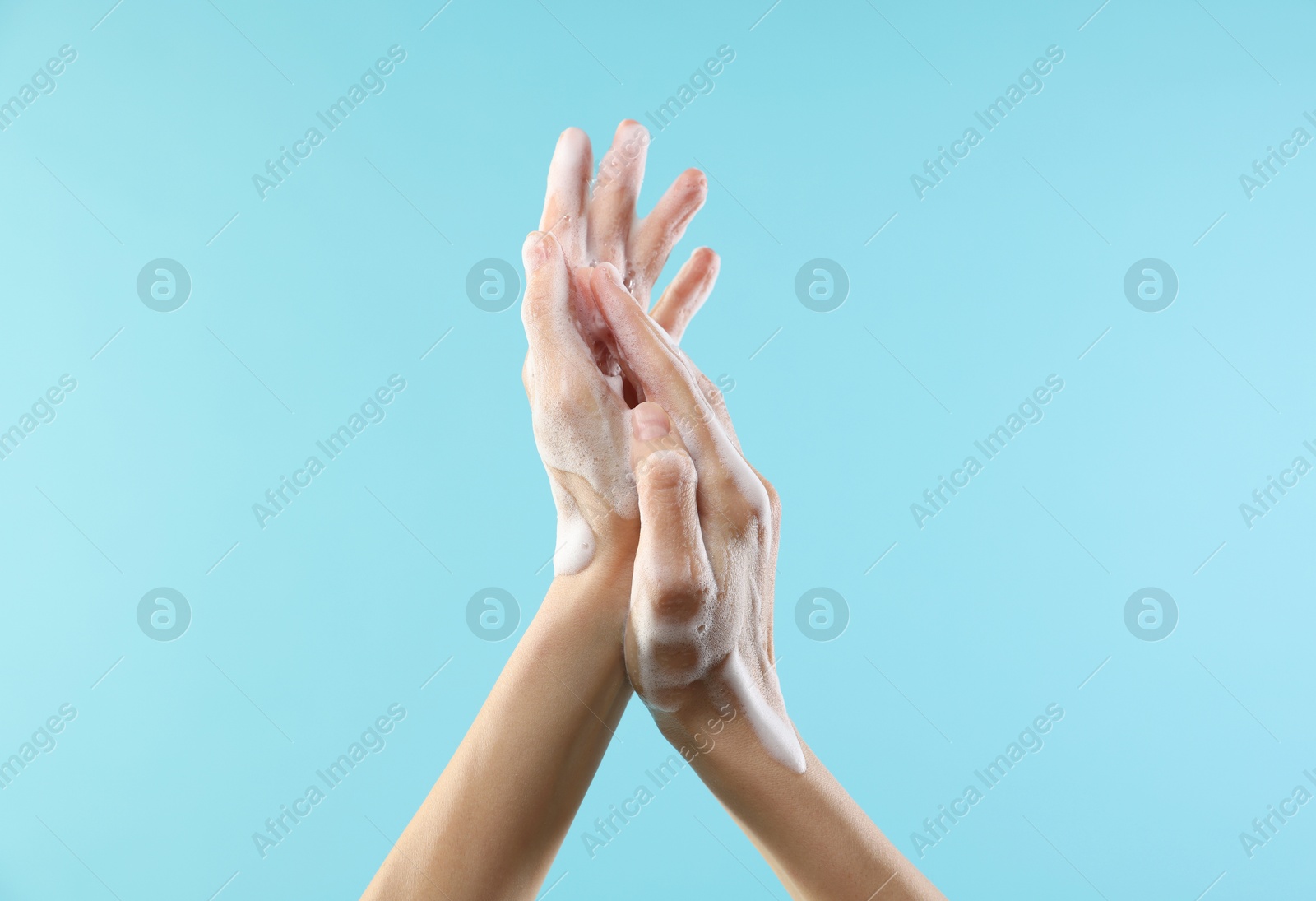 Photo of Woman washing hands with foaming soap on light blue background, closeup. Hygiene