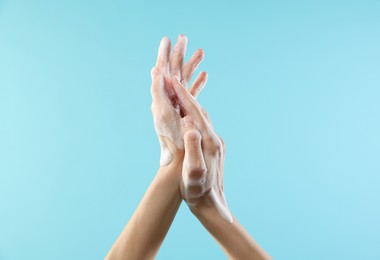 Woman washing hands with foaming soap on light blue background, closeup. Hygiene