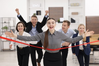 Competition concept. Happy businesswoman crossing red finish line ahead of her colleagues in office