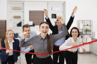 Photo of Competition concept. Happy businesswoman crossing red finish line ahead of her colleagues in office