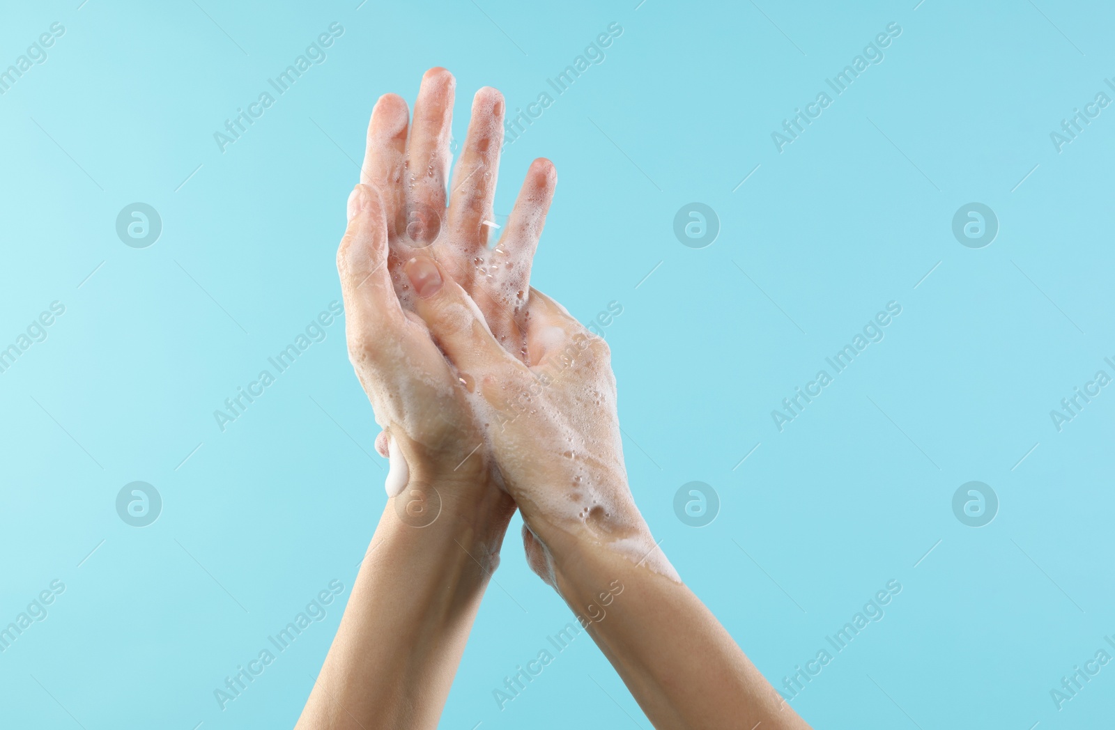 Photo of Woman washing hands with foaming soap on light blue background, closeup. Hygiene