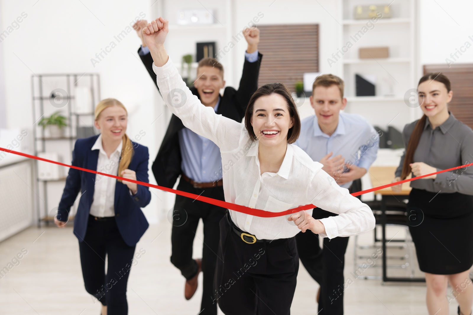 Photo of Competition concept. Happy businesswoman crossing red finish line ahead of her colleagues in office