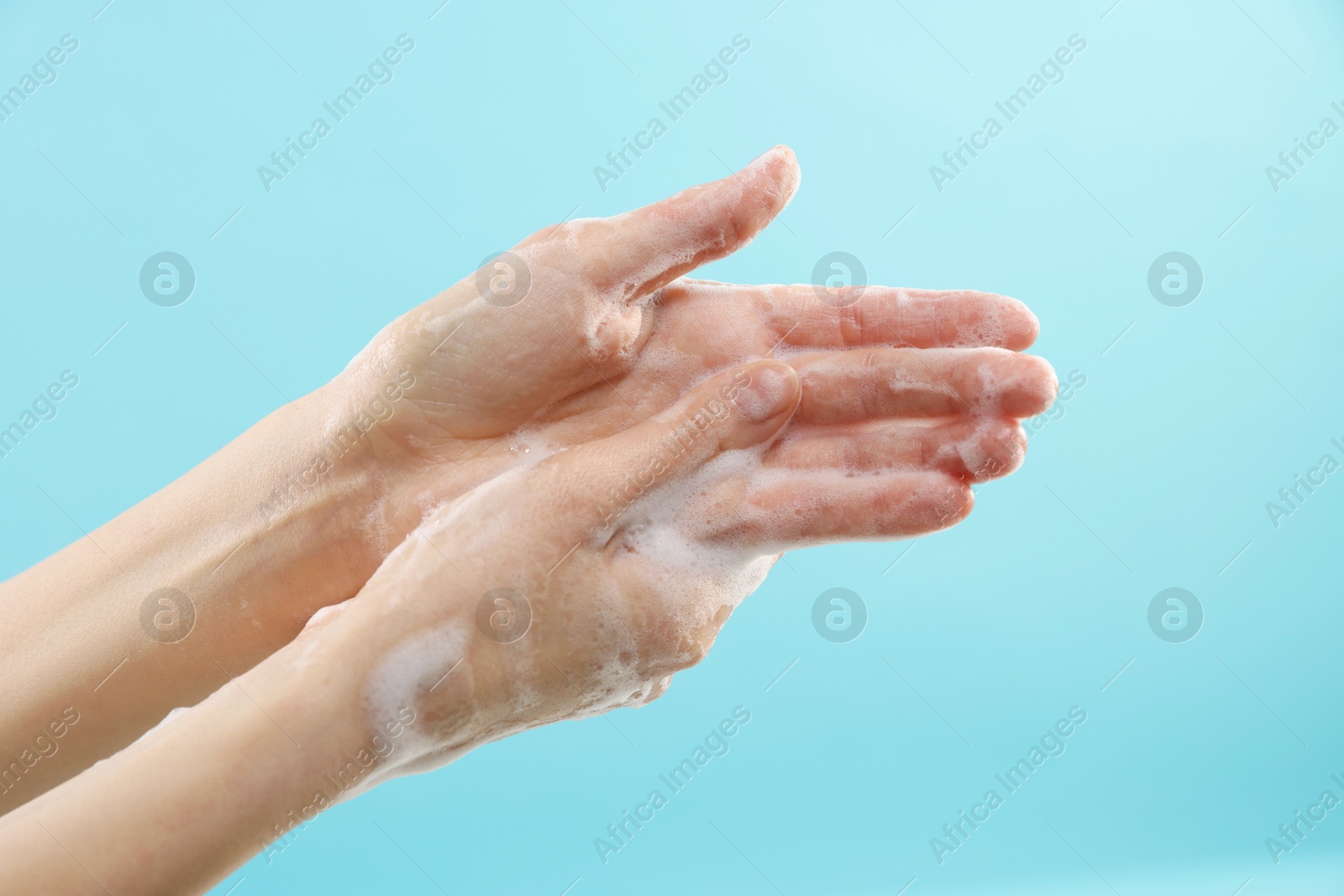 Photo of Woman washing hands with foaming soap on light blue background, closeup. Hygiene