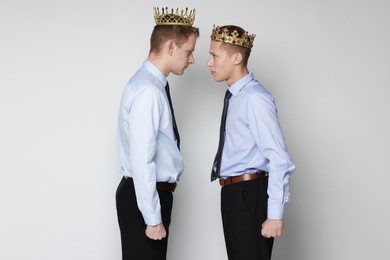 Business competition. Colleagues in golden crowns looking at each other on grey background