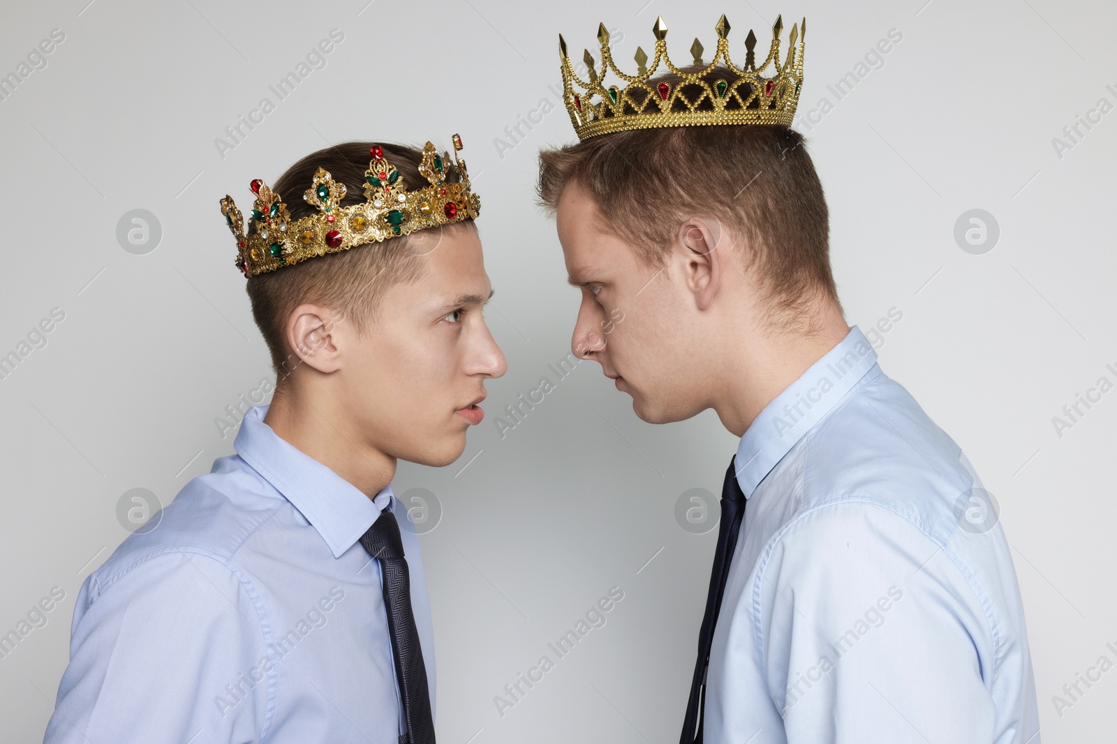 Photo of Business competition. Colleagues in golden crowns looking at each other on grey background