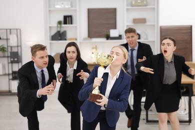 Photo of Competition concept. Businesswoman with trophy cup ahead of her colleagues in office