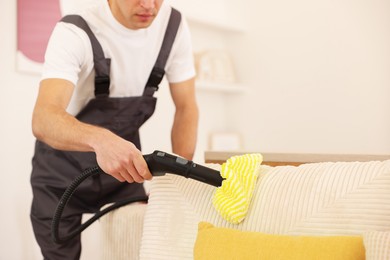 Photo of Professional janitor steam cleaning sofa in room, closeup