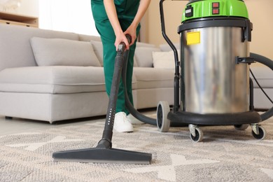 Photo of Professional cleaning service worker vacuuming rug indoors, closeup