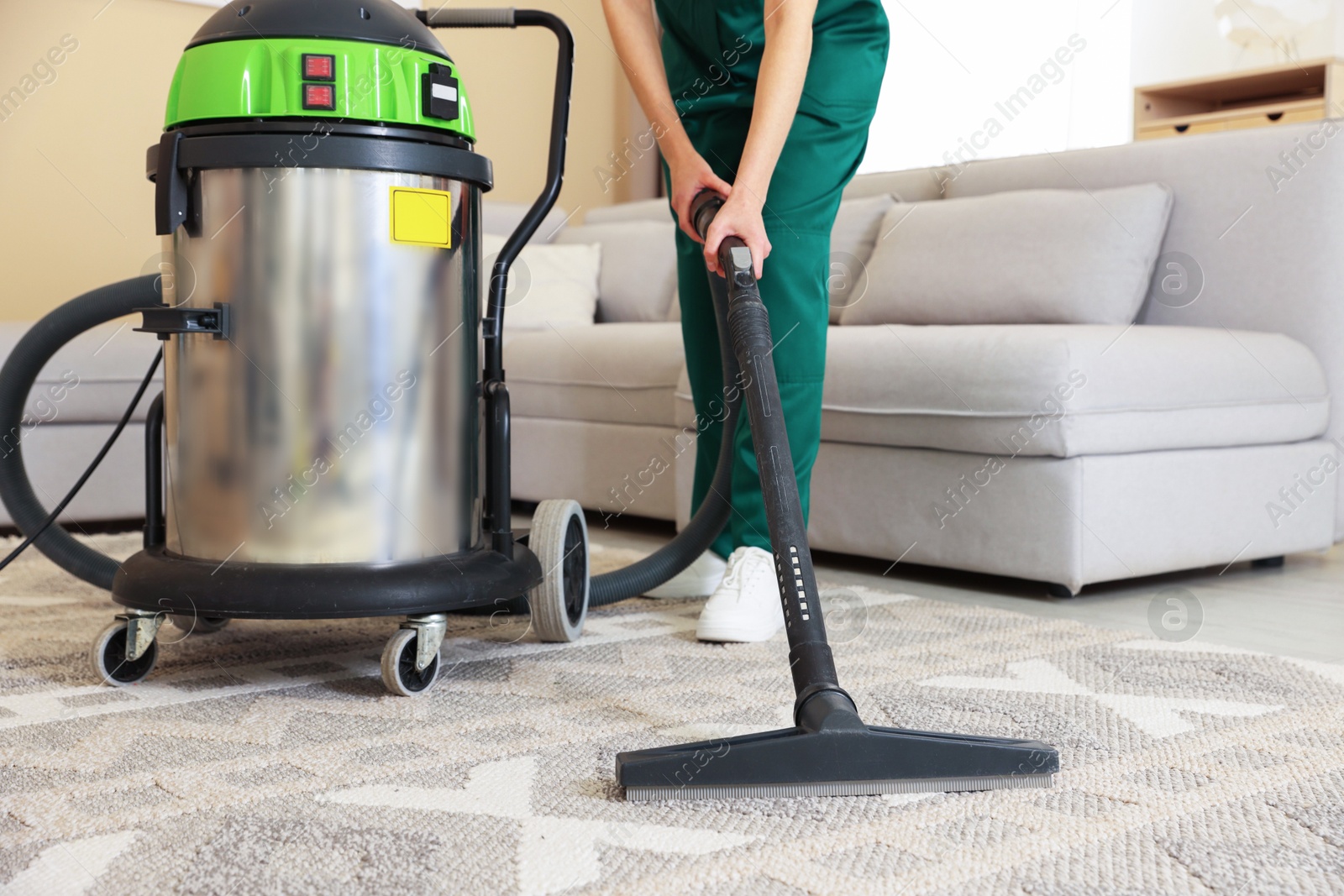 Photo of Professional cleaning service worker vacuuming rug indoors, closeup