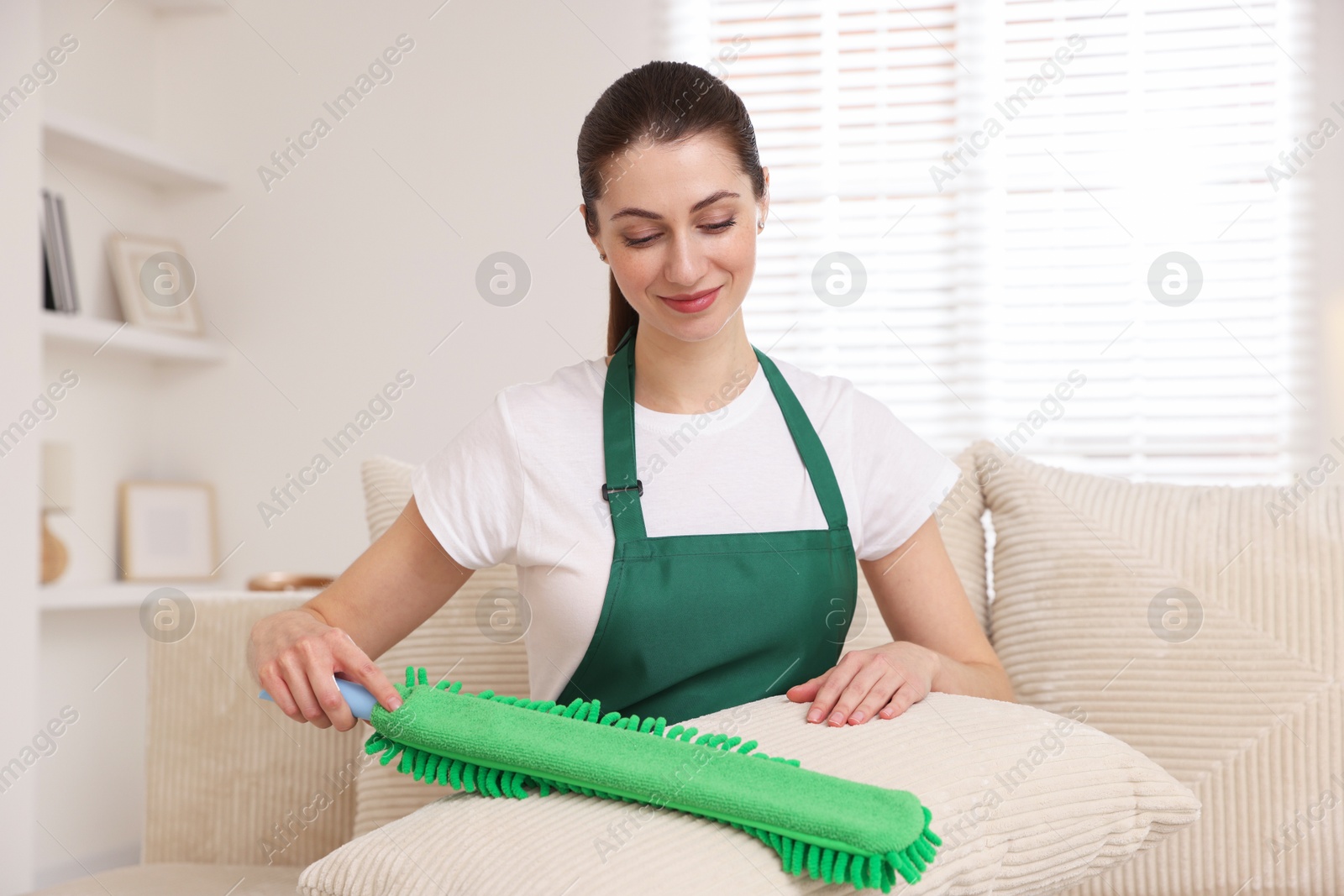 Photo of Janitor cleaning sofa cushion with duster at home