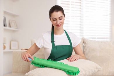 Janitor cleaning sofa cushion with duster at home