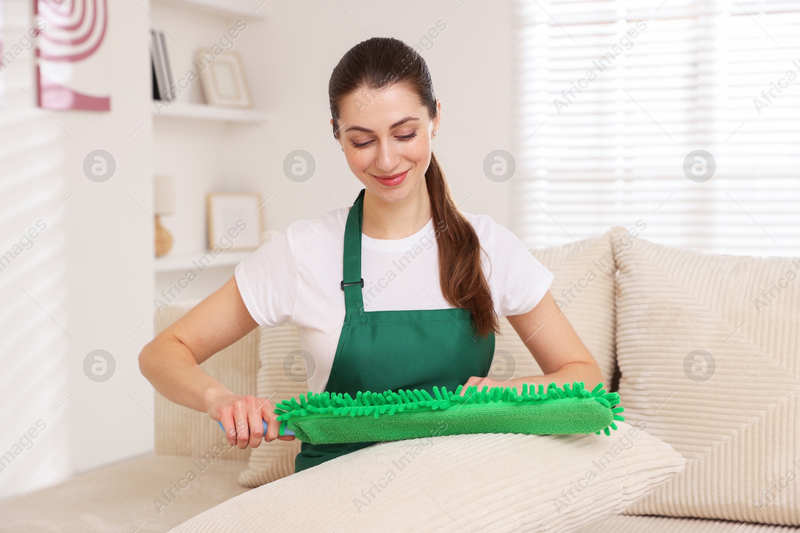 Photo of Janitor cleaning sofa cushion with duster at home