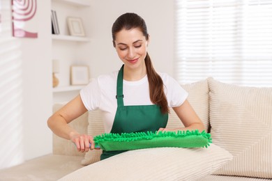 Janitor cleaning sofa cushion with duster at home