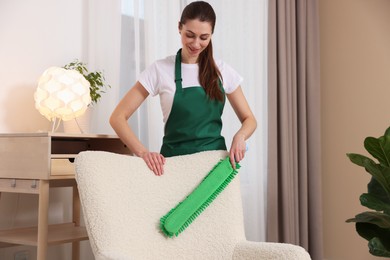 Photo of Janitor cleaning armchair with duster at home