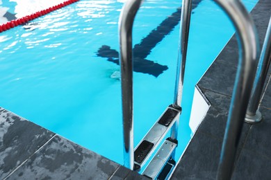 Swimming pool with clean water and ladder indoors, closeup