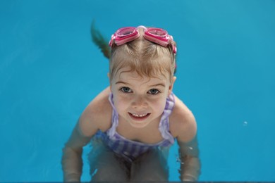 Photo of Little girl with goggles swimming in pool, above view