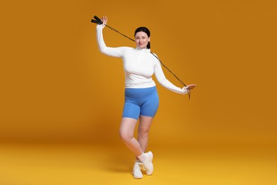 Plus size woman in gym clothes with skipping rope on orange background