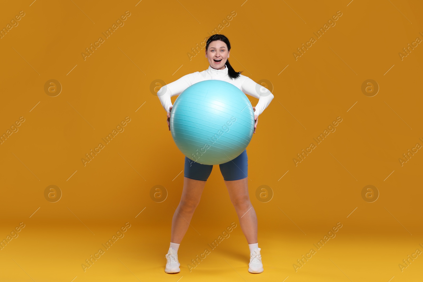 Photo of Plus size woman in gym clothes with fitness ball on orange background