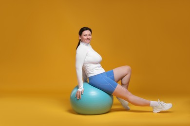 Photo of Plus size woman in gym clothes with fitness ball on orange background