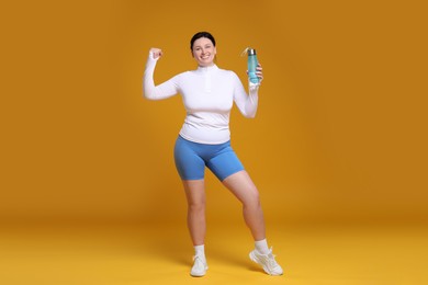 Photo of Plus size woman in gym clothes with water bottle on orange background