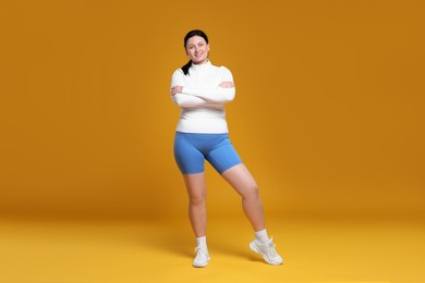 Plus size woman in gym clothes on orange background