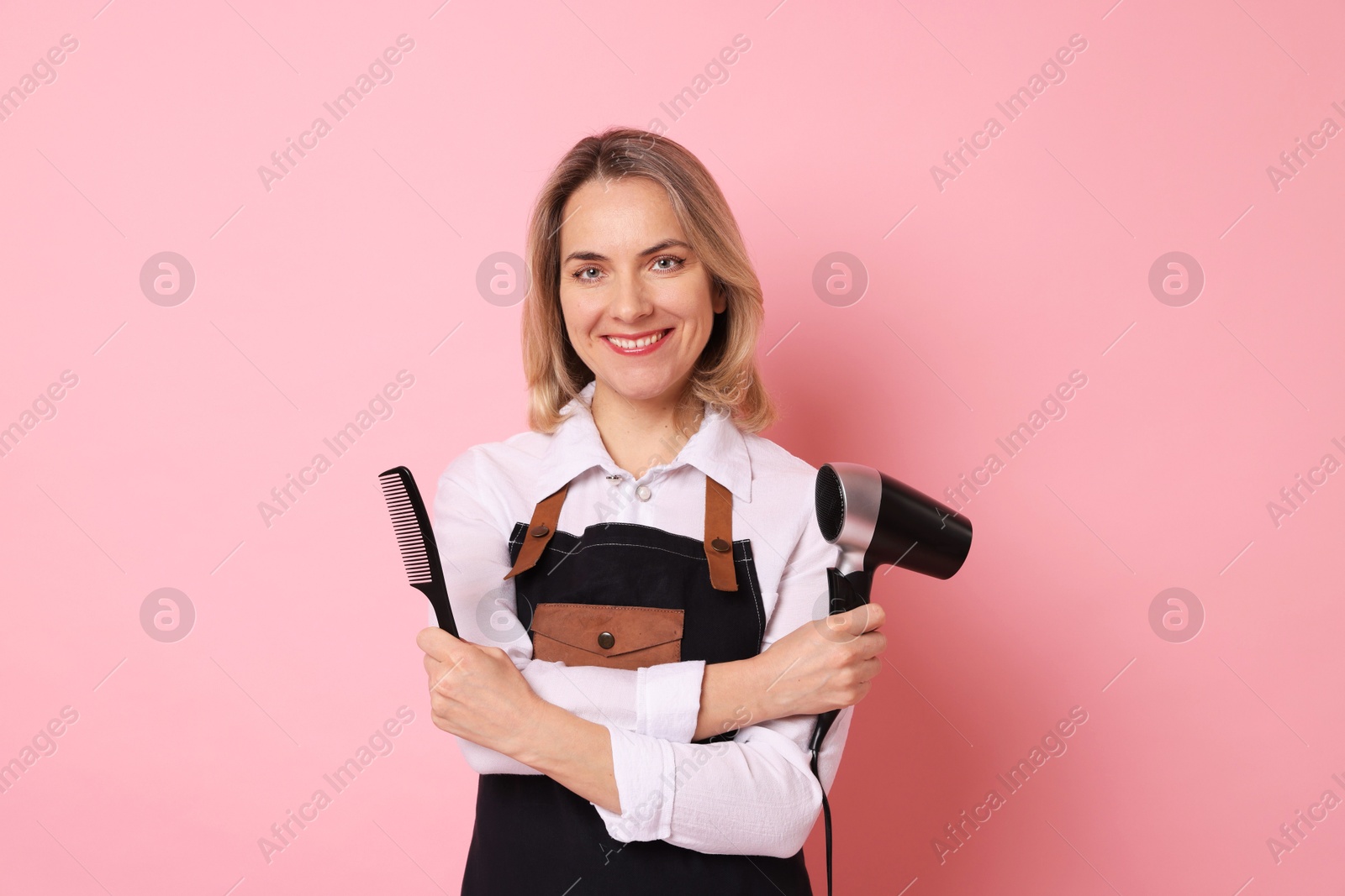 Photo of Smiling hairdresser with dryer and comb on pink background