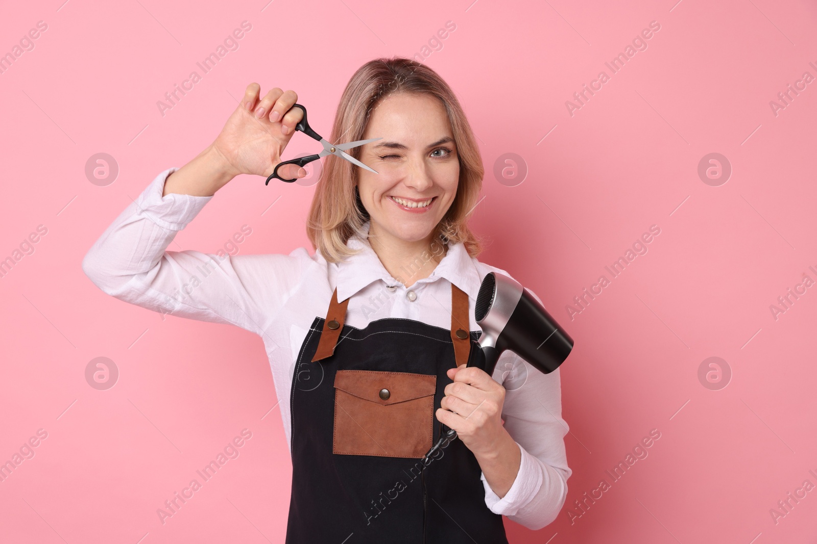 Photo of Smiling hairdresser with dryer and scissors on pink background