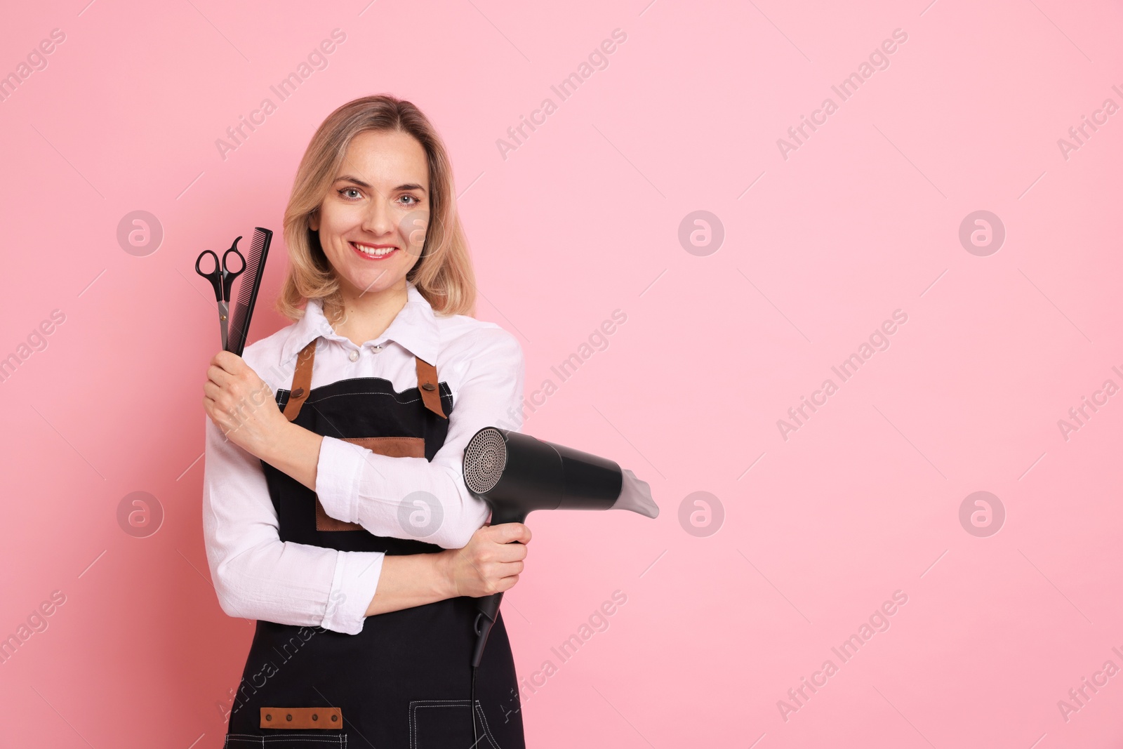 Photo of Smiling hairdresser with dryer, scissors and comb on pink background, space for text