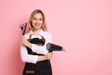 Photo of Smiling hairdresser with dryer, scissors and comb on pink background, space for text