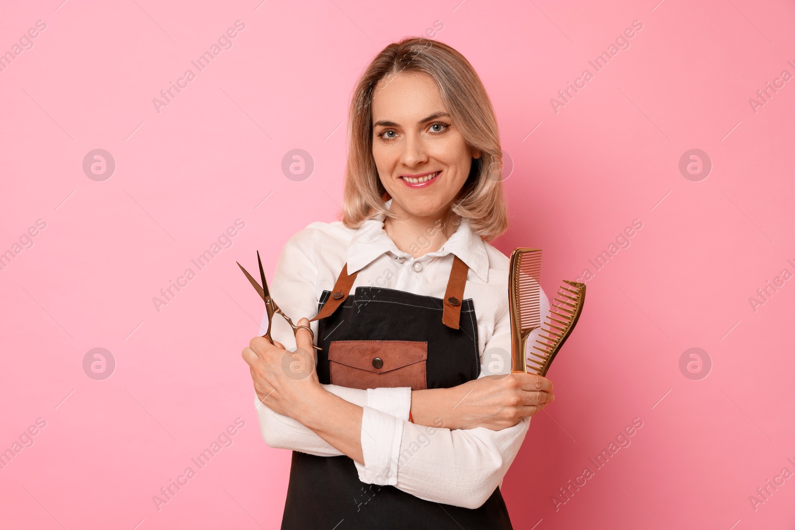 Photo of Smiling hairdresser with combs and scissors on pink background