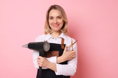 Photo of Smiling hairdresser with dryer and scissors on pink background